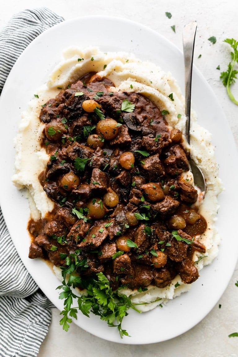 beef tips with gravy served over mashed potatoes on white serving platter