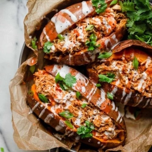 Three buffalo chicken stuffed sweet potatoes with ranch dressing in a round serving tray.