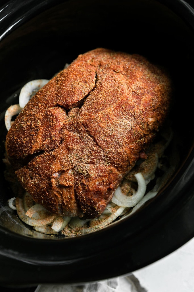 A pork butt rubbed with seasoning in a slow cooker for shredded pork.