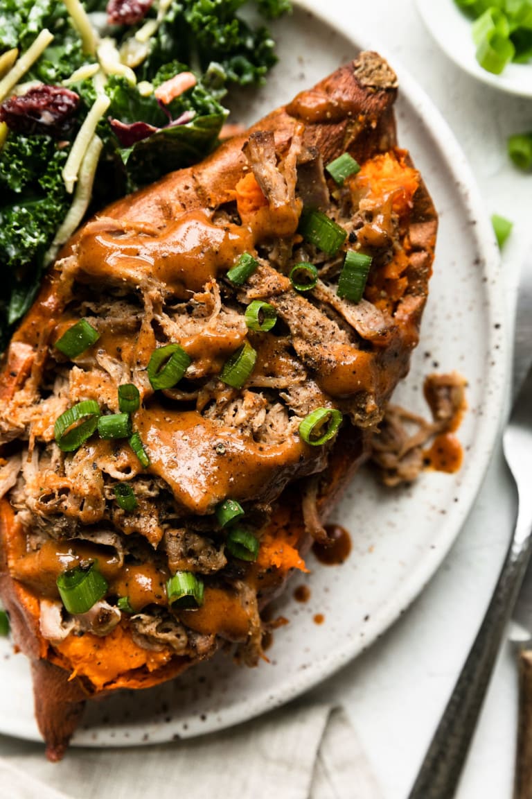 Overhead view of a plate of sweet potatoes topped with pulled pork and honey mustard BBQ sauce.