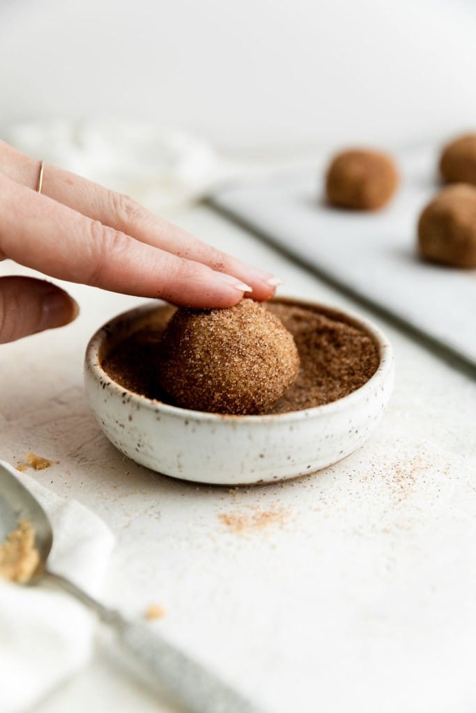A Snickerdoodle cookie dough ball being rolled in cinnamon sugar.