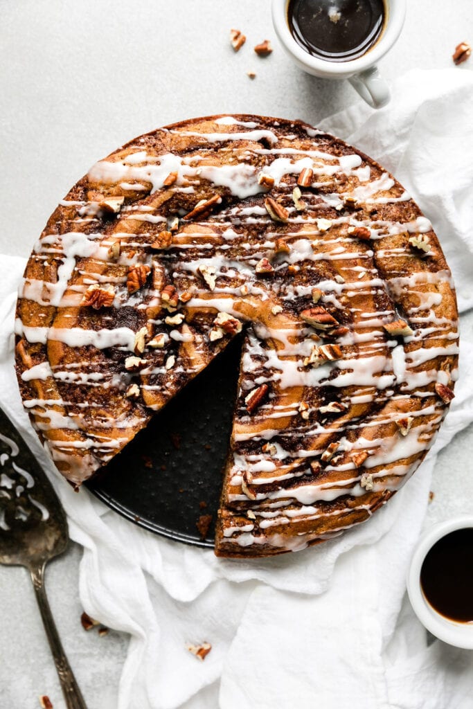 Overhead view round cinnamon roll coffee cake drizzled with white glaze and sprinkled with chopped pecans.