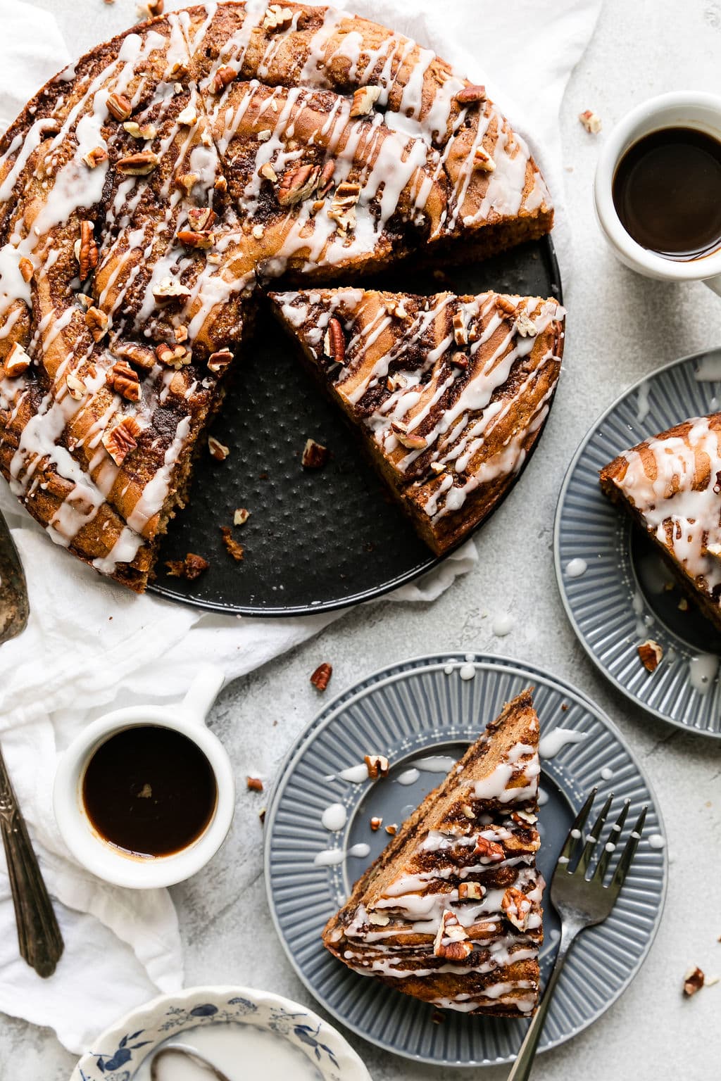 Overhead view round gluten free cinnamon roll coffee cake with slices removed. Slices of coffee cake on blue plates. 