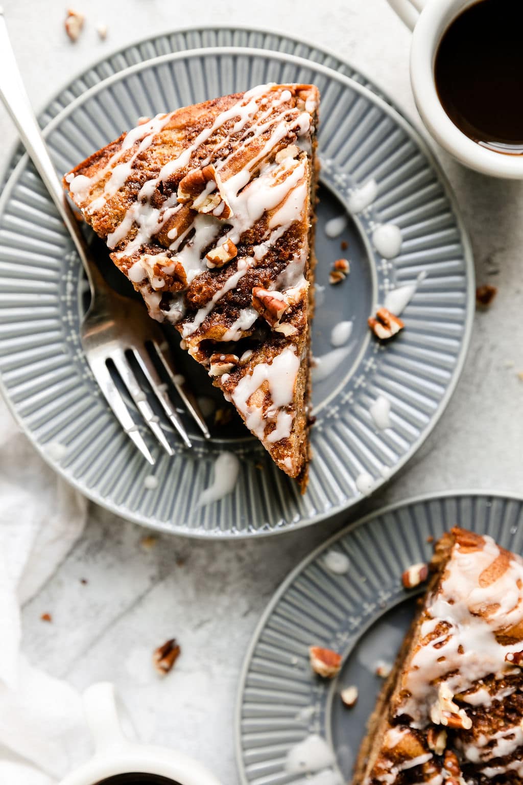 A single slice cinnamon roll coffee cake with white glaze drizzle on top on a blue plate with silver fork resting on plate.