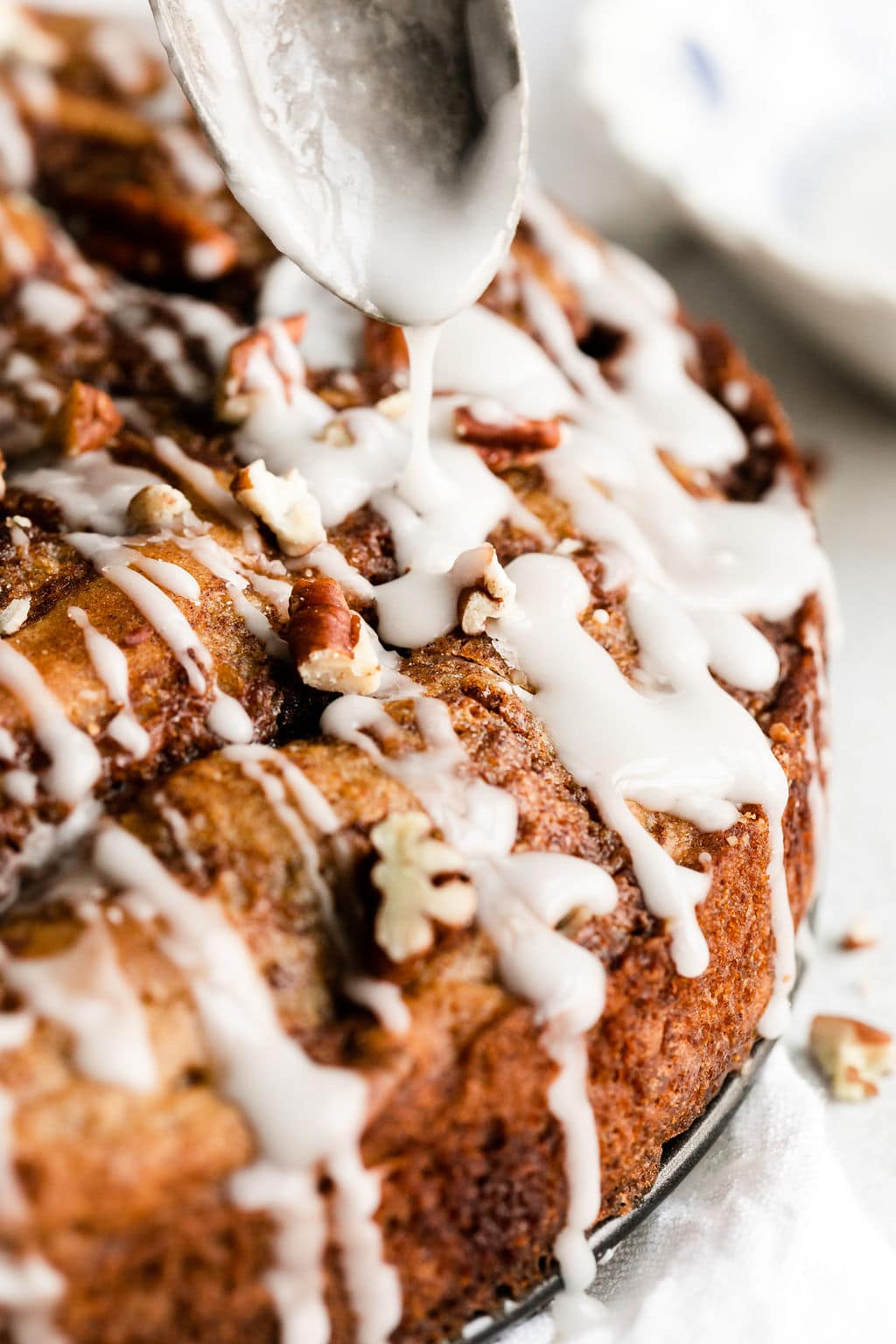 Close up view white glaze being drizzled over round cinnamon roll coffee cake.