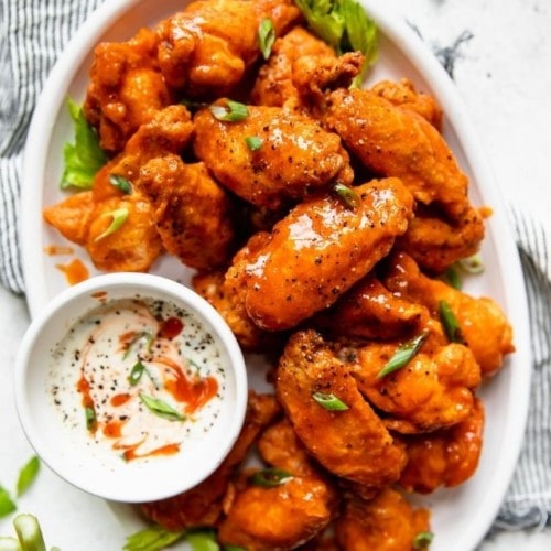 Overhead view of crispy baked buffalo wings on a white platter with a side of ranch dressing.