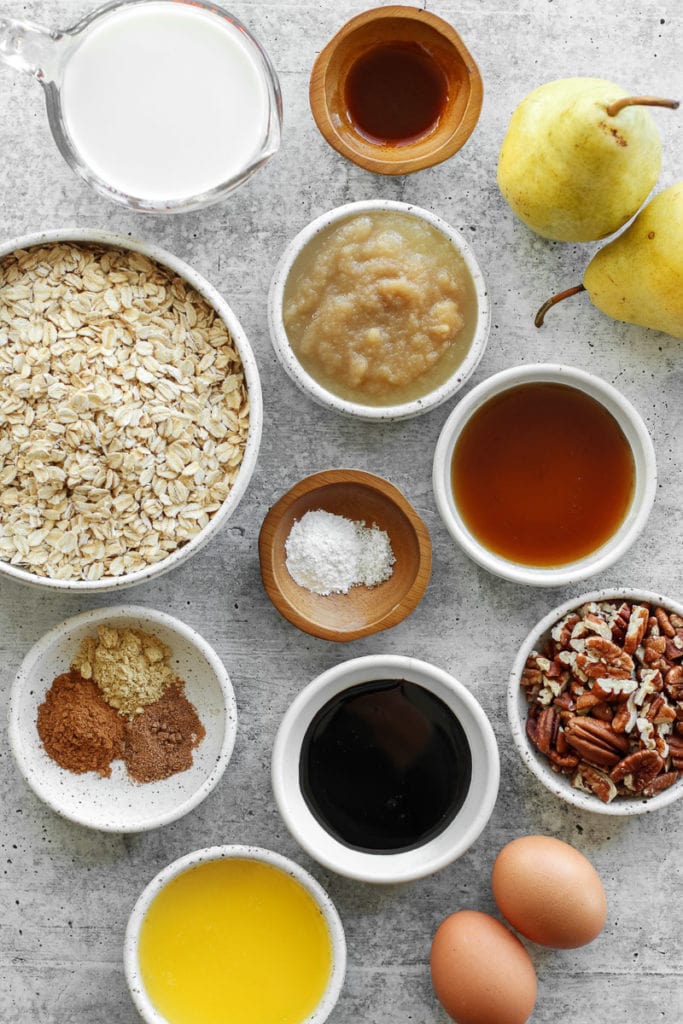 All ingredients for gingerbread oatmeal arranged in small bowls with whole pears on the side.