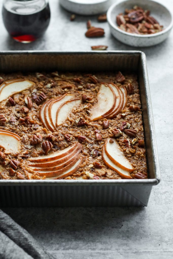 Gingerbread baked oatmeal with pears and pecans arranged on top all in a square baking pan.