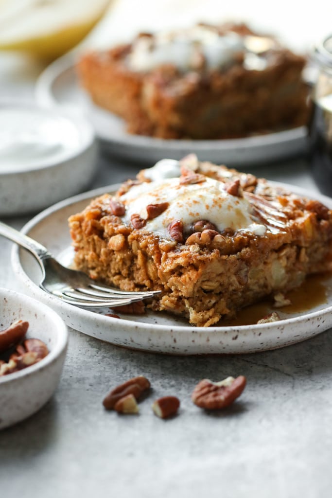 A square of gingerbread baked oatmeal on a speckled plate topped with pecans and whipped cream.