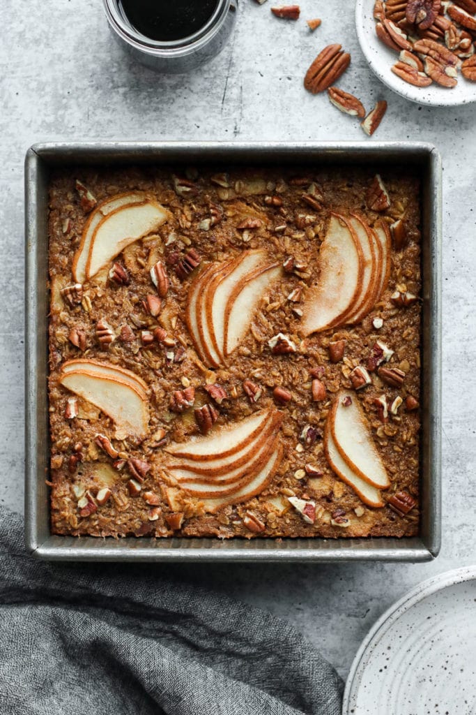 Overhead view of gingerbread baked oatmeal in a square baking pan with pears arranged on top with pecan pieces scattered around on top.