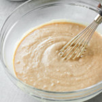 The batter for cinnamon roll coffee cake in a clear glass bowl with a whisk