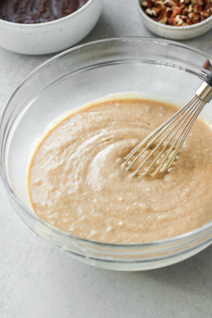 The batter for cinnamon roll coffee cake in a clear glass bowl with a whisk