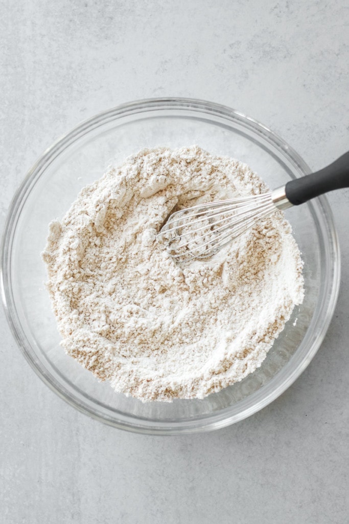 Dry ingredients for cinnamon roll coffee cake in a clear glass bowl with a whisk