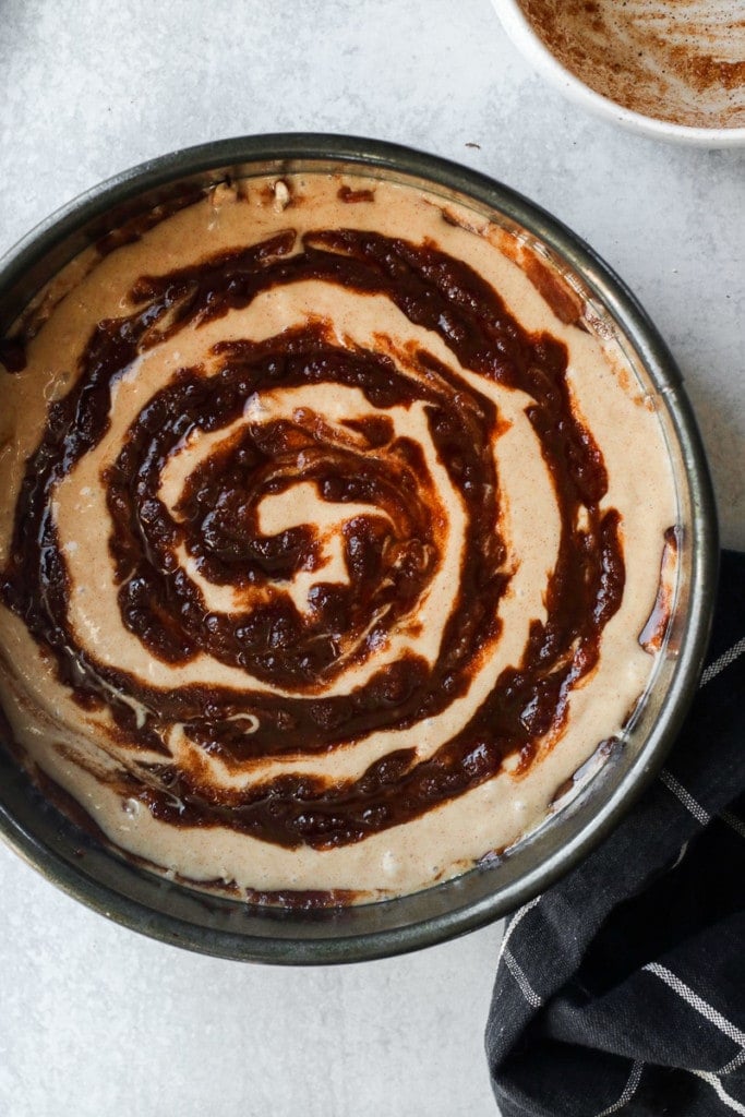 Overhead view of cinnamon roll coffee cake in a round cake pan with cinnamon mixture swirled into the top