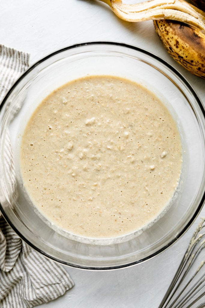 Overhead view of banana oatmeal pancake batter in a glass mixing bowl