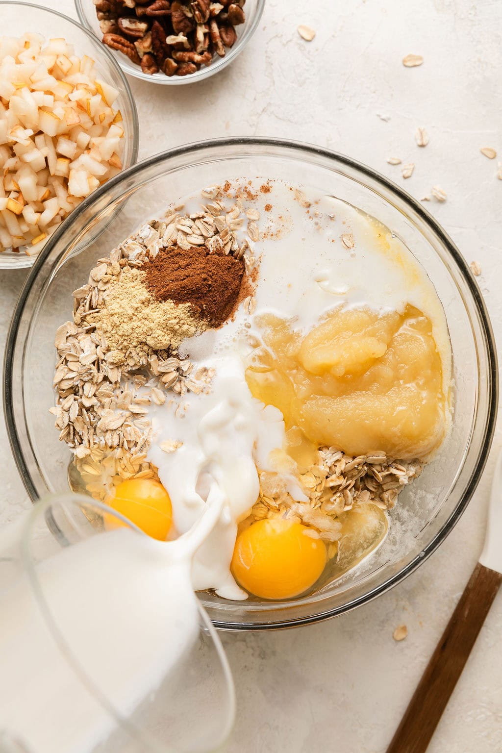 Overhead view of a glass bowl filled with baked oatmeal ingredients and milk being poured on top.
