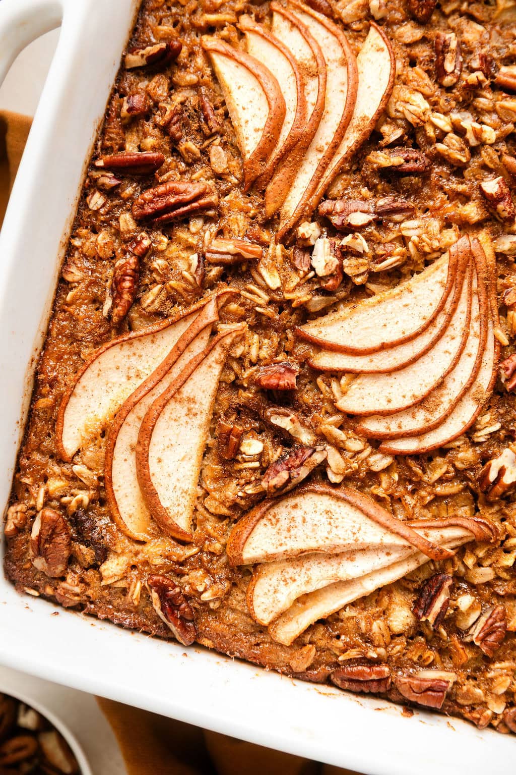 Close up view of a white baking dish filled with Gingerbread Baked Oatmeal topped with thinly sliced pears and pecan pieces.