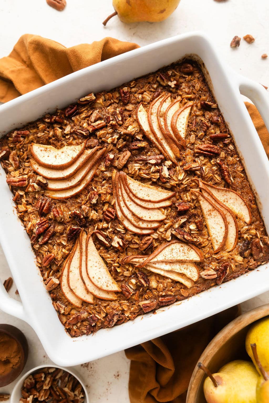 Overhead view of a white baking dish filled with Gingerbread Baked Oatmeal topped with thinly sliced pears and pecan pieces. 