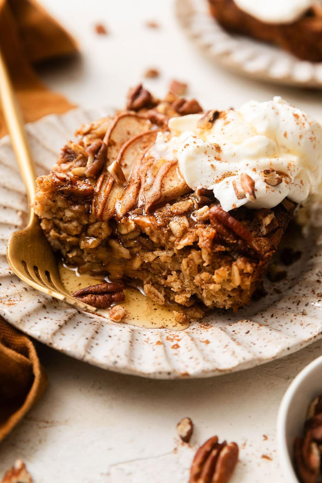 Close up view of a piece of Gingerbread Baked Oatmeal on a plate topped with a dollop of whipped cream and drizzled with maple syrup.