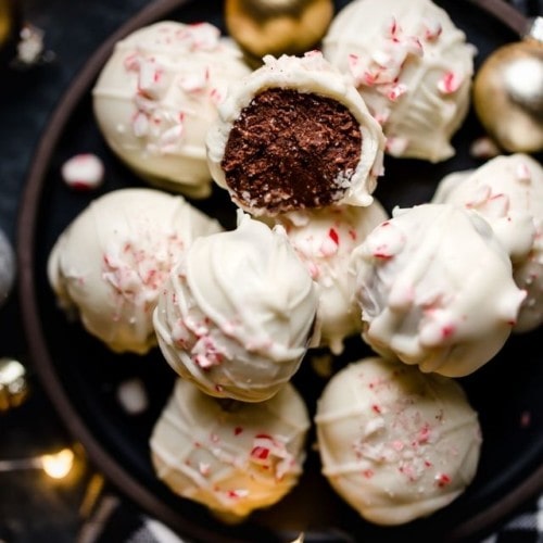 Close up view of a brownie batter truffle coated in white chocolate and sprinkled with peppermint flecks stacked high on a tray of truffles.