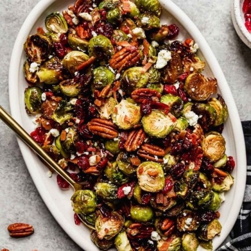 Roasted brussels sprouts with bacon, balsamic, feta, and dried cranberries on a white platter.