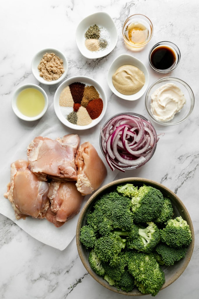All ingredients for sheet pan chicken thighs with broccoli and honey mustard sauce arranged together in small bowls. 