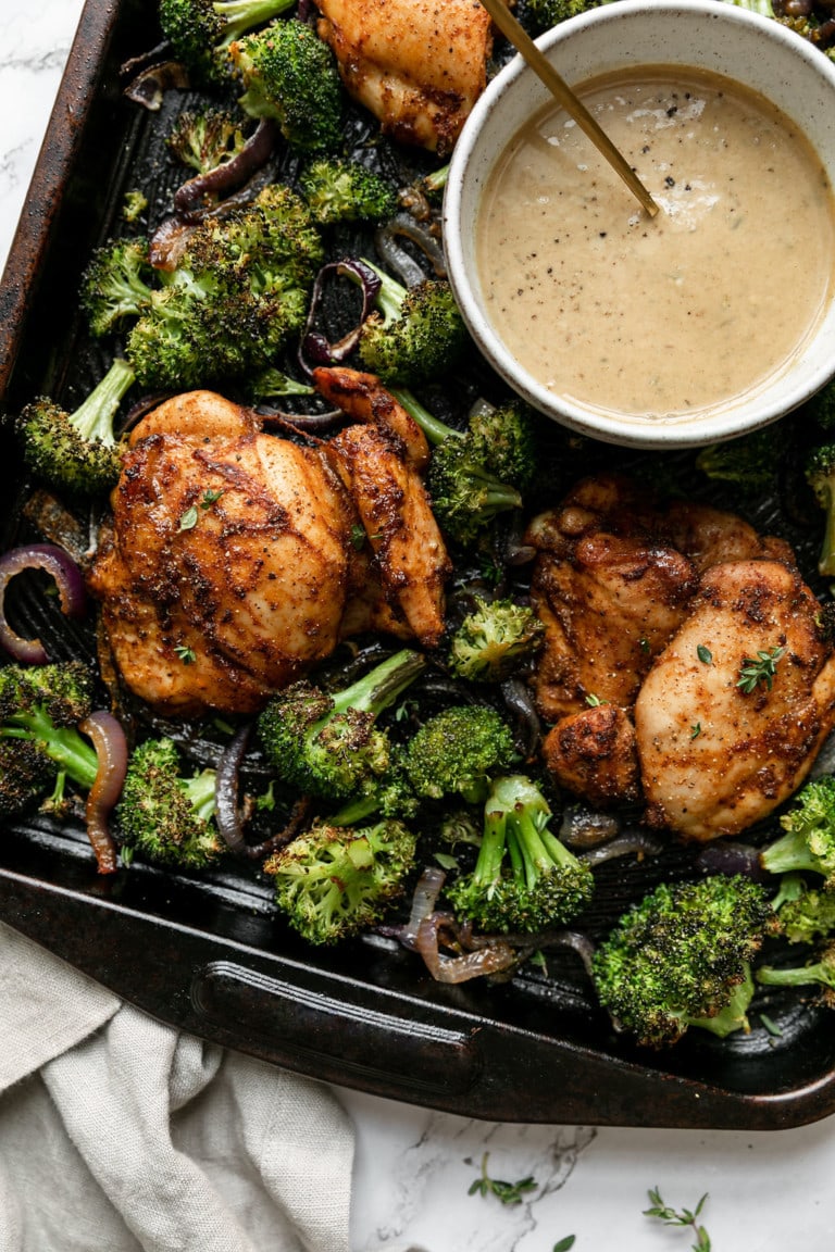 Overhead view sheet pan chipotle chicken thighs with broccoli, side of honey mustard sauce.
