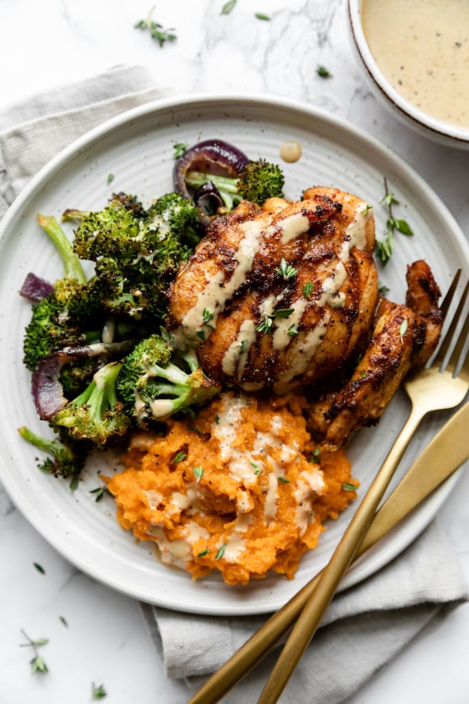 Overhead view of chipotle chicken thigh plated on a white plate with side of broccoli and mashed sweet potatoes, drizzled with honey mustard sauce.