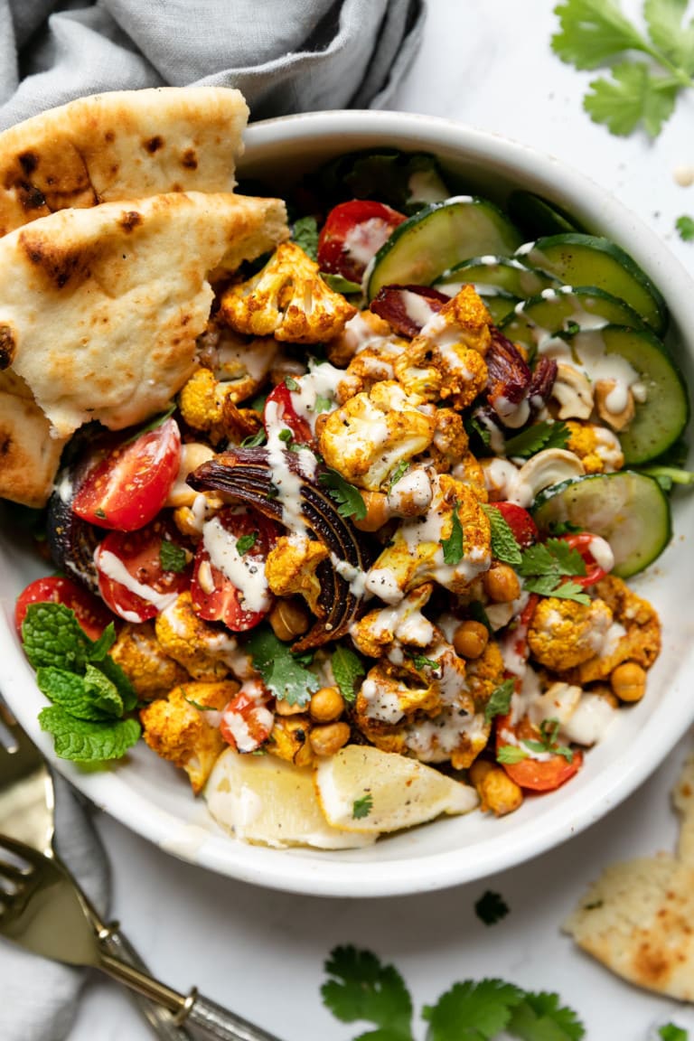 A bowl of sheet pan veggie shawarma topped with lemon tahini dressing. Served with naan bread. 