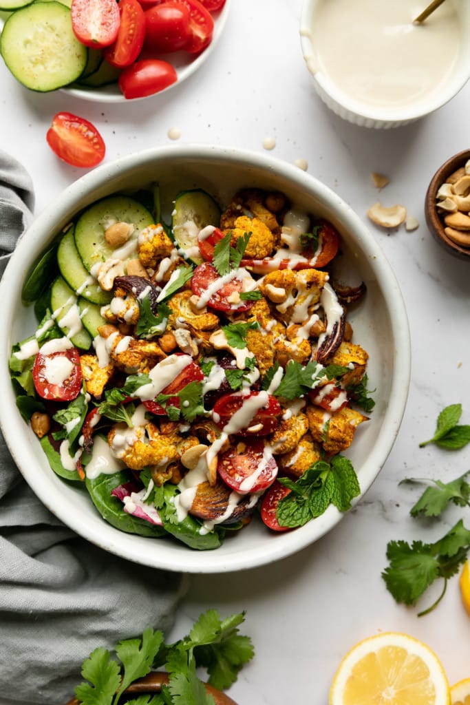 Bowl of Veggie Shawarma With Lemon Tahini Dressing next to fresh cut vegetables and lemons. 