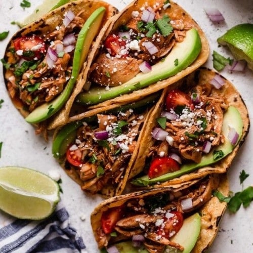 Several slow cooker chicken tacos in corn shells topped with fresh cilantro and avocado slices.