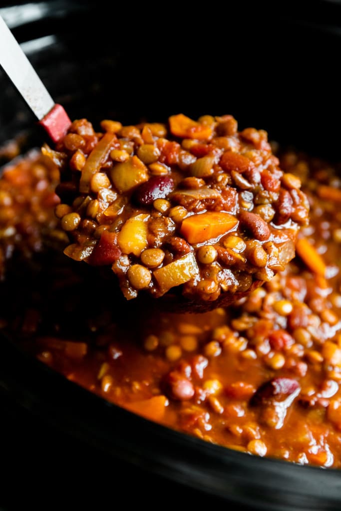 A ladle lifting out a heaping serving of slow cooker vegan lentil chili