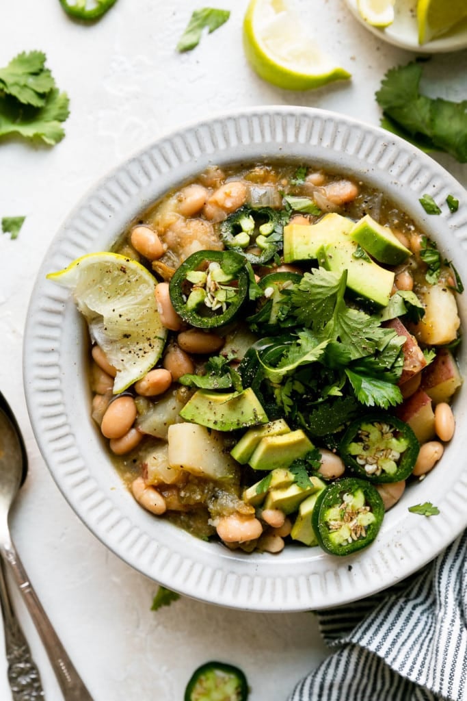 Close up overhead view of slow cooker green chile stew with white beans and potatoes in a white bowl