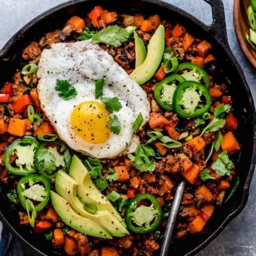 Overhead view of tex-mex sweet potato hash in a cast iron skillet with a fried egg on top