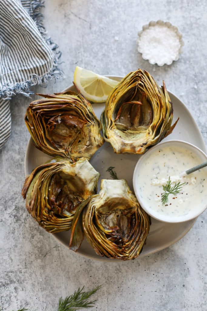 Overhead view of air fried artichoke halves on a white platter with a side of feta yogurt dip.