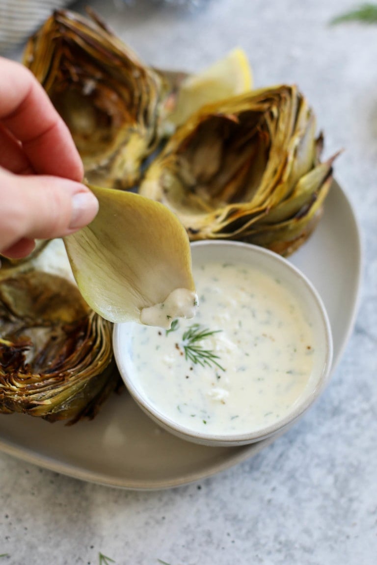 Close up view of a hand dipping a piece of artichoke into a feta yogurt dip.