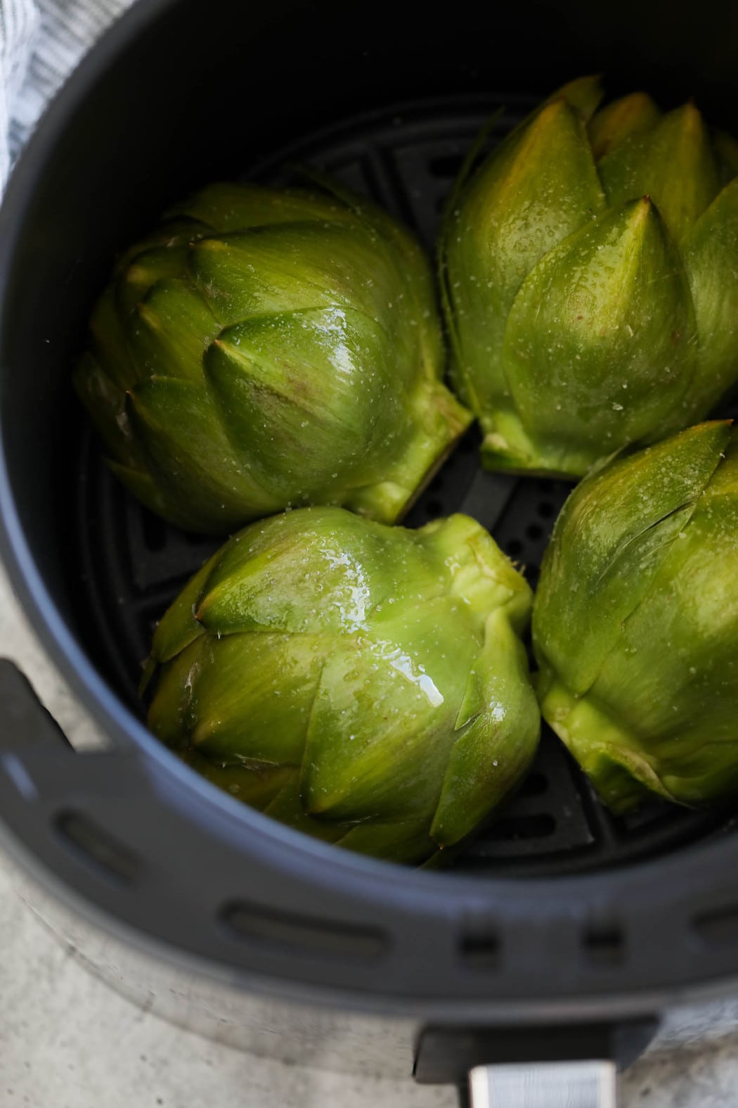 Four artichoke halves in an air fryer basket cut side down.