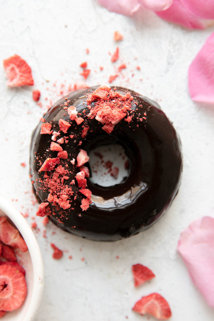 Overhead view of chocolate donut with chocolate icing, crushed dried strawberries on half of donut icing.