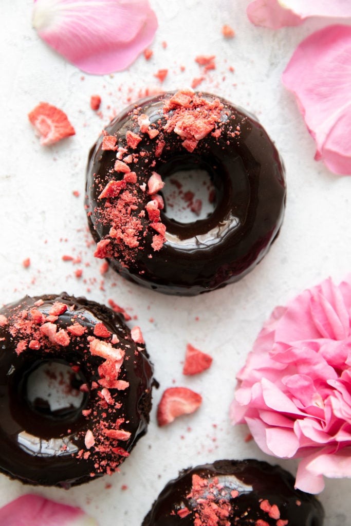 Overhead view of chocolate flourless donuts with thin chocolate icing and crushed dried strawberries sprinkled on top.