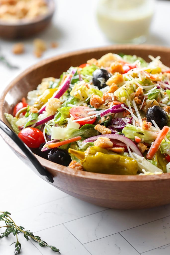 Close up view of copycat Olive Garden Salad in a wooden serving bowl topped with fresh parmesan, red onion, pepperoncinis, and tomatoes.