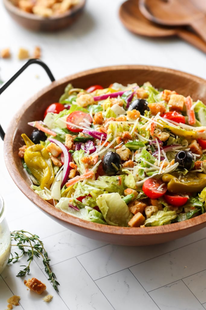 Overhead view of Olive Garden inspired side salad with parmesan, olives, pepperoncinis, and red onions in a wooden serving bowl. 