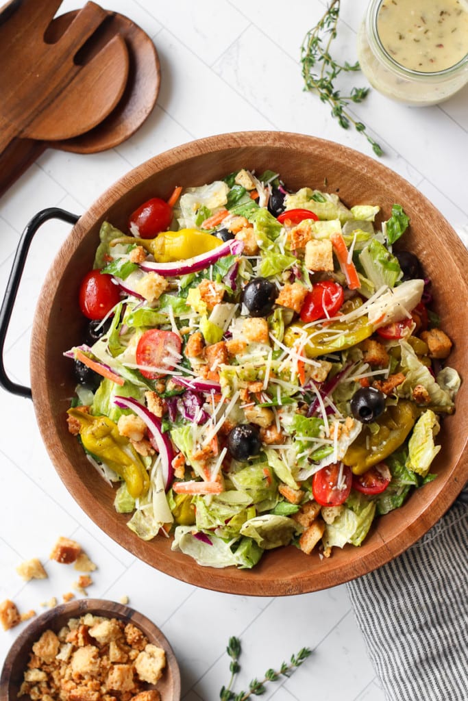 Overhead view of copycat Olive Garden Salad in a wooden bowl topped with gluten-free croutons, parmesan cheese, fresh tomatoes, and homemade dressing.