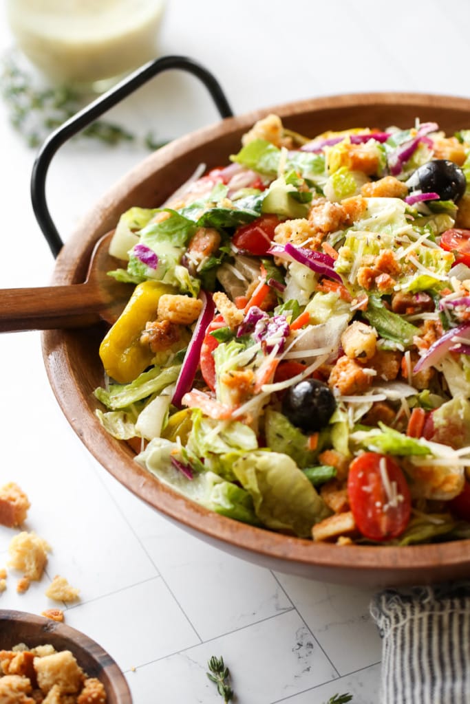 A copycat Olive Garden Salad with Creamy Italian Dressing in a wooden serving bowl topped with croutons and parmesan.