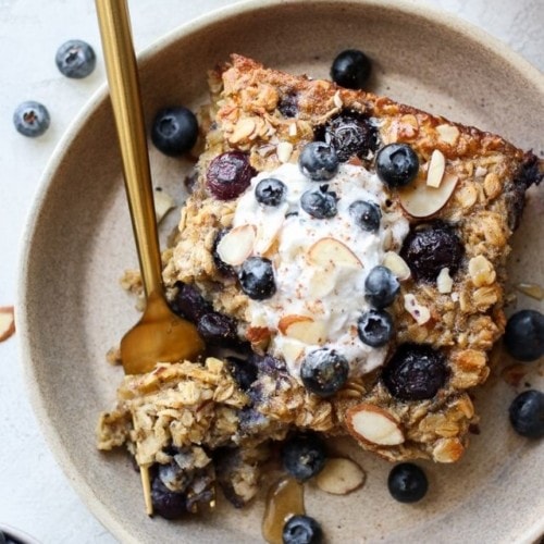 Overhead view of healthy blueberry baked oatmeal on a plate topped with whipped cream and fresh blueberries.