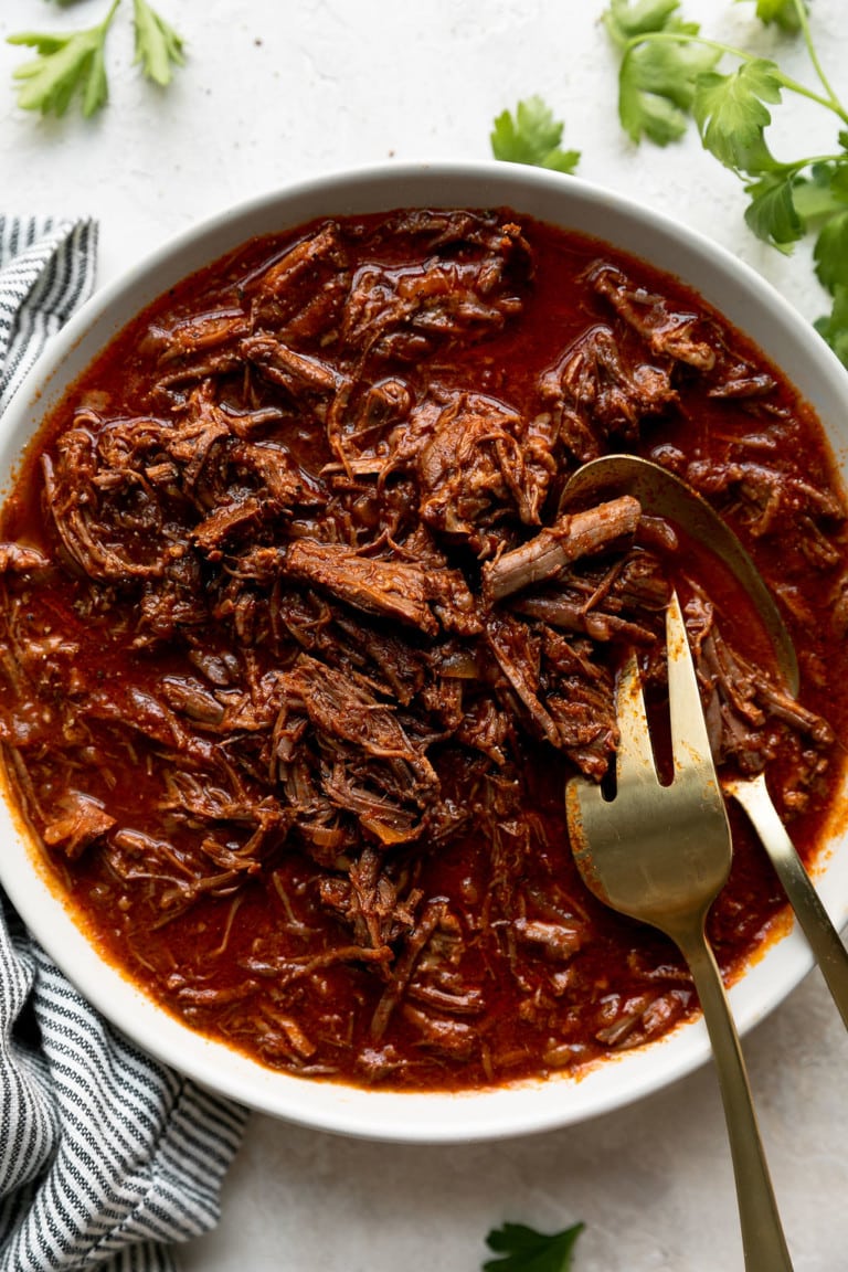 Overhead view shredded slow cooker bbq beef in white serving bowl with gold serving fork.