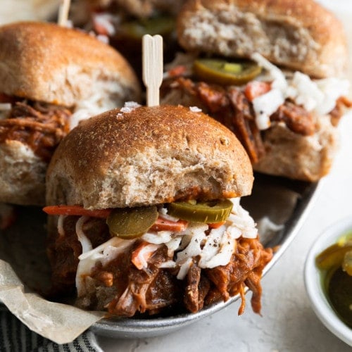 Four Instant Pot Shredded Beef Sliders filled with beef, coleslaw, jalapenos in a wheat bun with a toothpick on top.