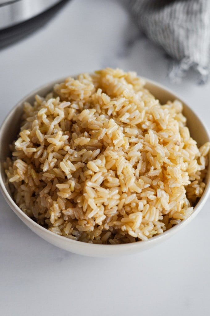 Close up view of fluffy brown rice in a cream colored bowl with an Instant Pot in the background.