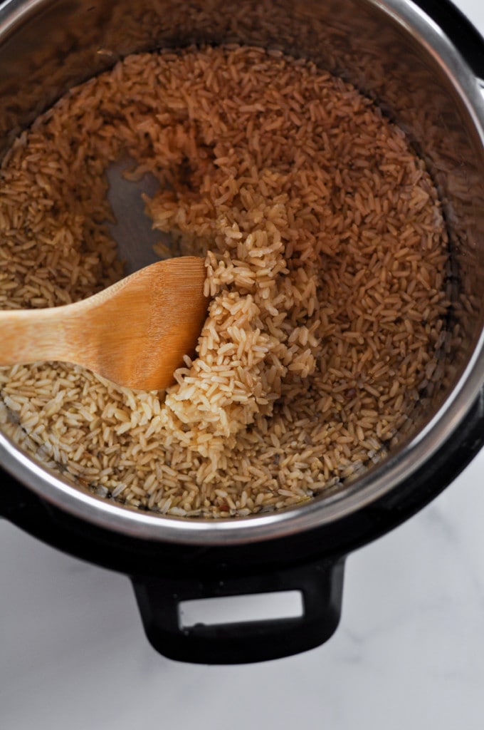 A wooden spoon in an Instant Pot stirring freshly made brown rice.