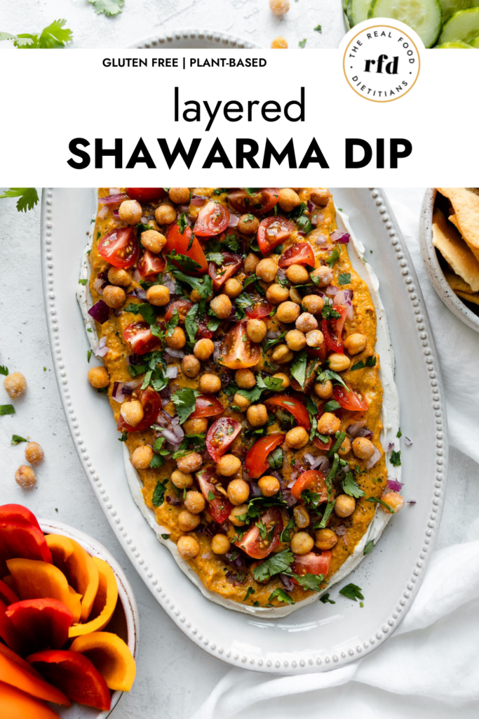 Overhead view of layered Shawarma Dip on a white platter, fresh cut veggies on the side.