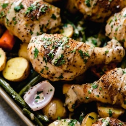 Close up view of Caesar coated chicken legs over roasted veggies on a sheet pan.